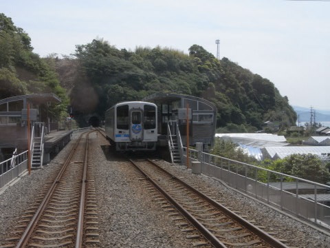 行く先のトンネルの上の山に崖崩れの跡の残る穴内駅に停まるごめん・なはり線の列車