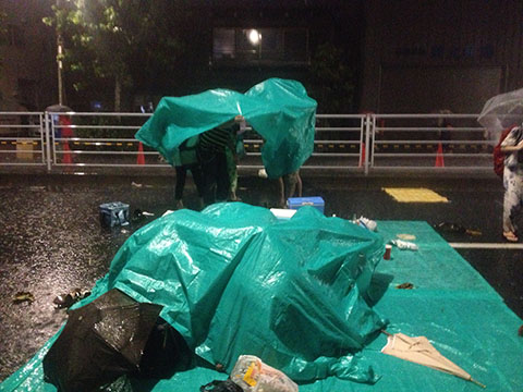 隅田川花火大会の途中で降り始めた雷雨にビニールシートをかぶって雨を凌ぐ人